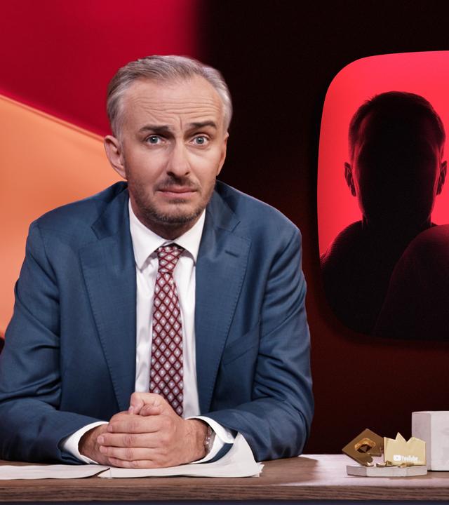 Jan Böhmermann sitzt am Schreibtisch. Rechts neben ihm ist eine Darstellung von drei gesichtslosen Silhouetten vor einem roten Hintergrund abgebildet.