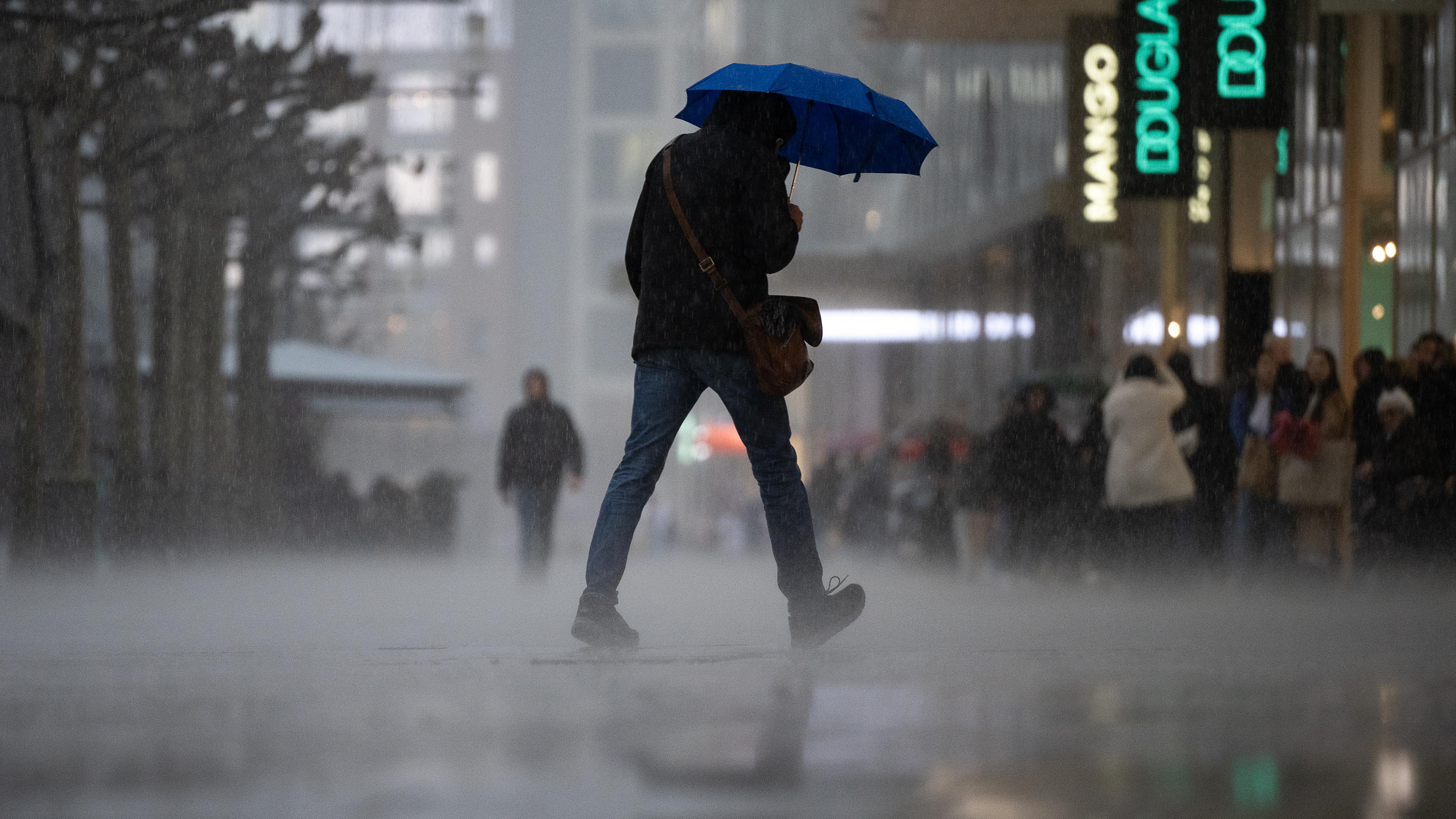 Hessen, Frankfurt/Main: Ein Mann geht während eines starken Regengusses auf der Frankfurter Einkaufsstraße Zeil über die Straße.