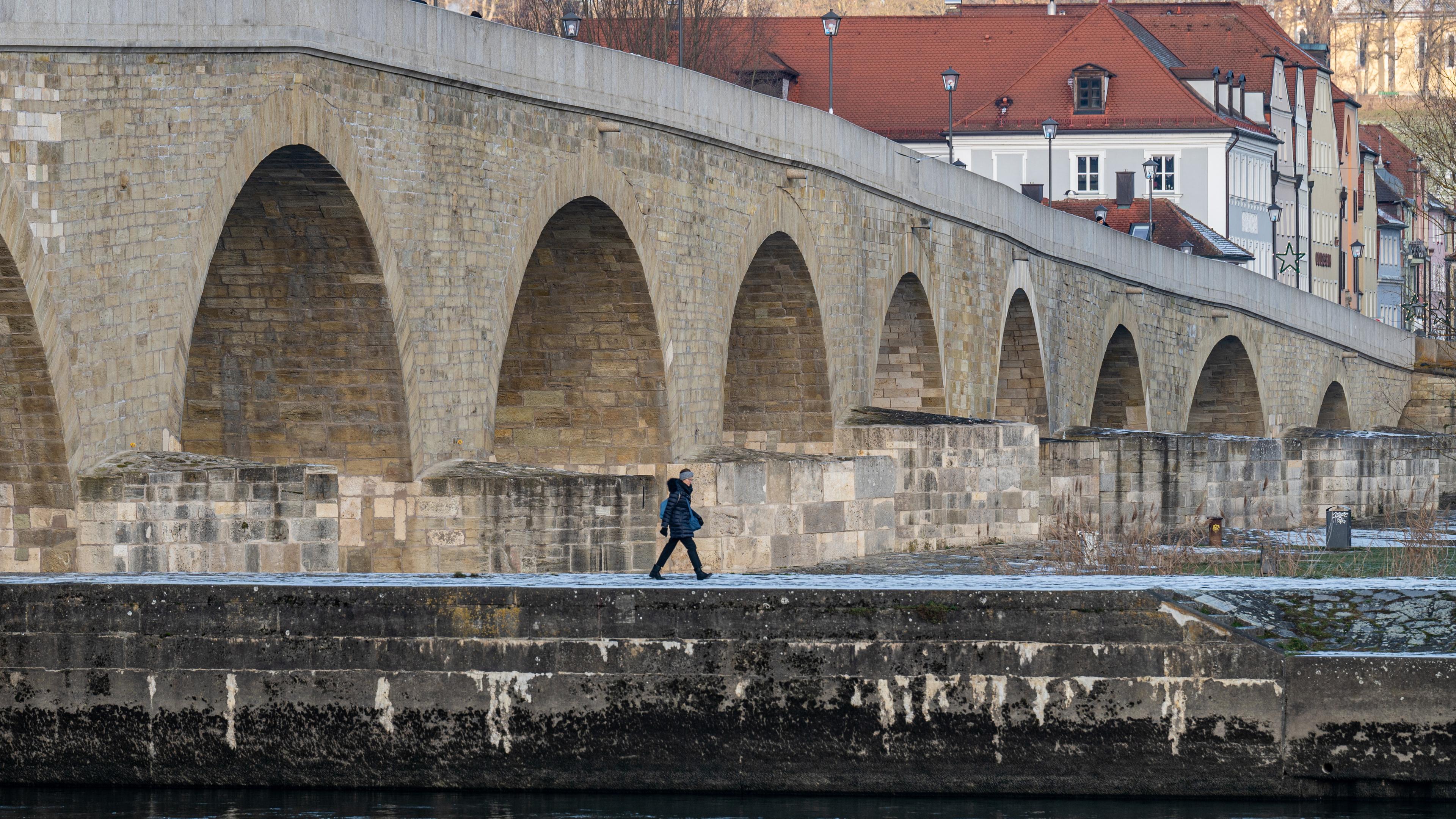 Bayern, Regensburg: Eine Spaziergängerin ist bei kaltem Winterwetter vor der Steinernen Brücke unterwegs.