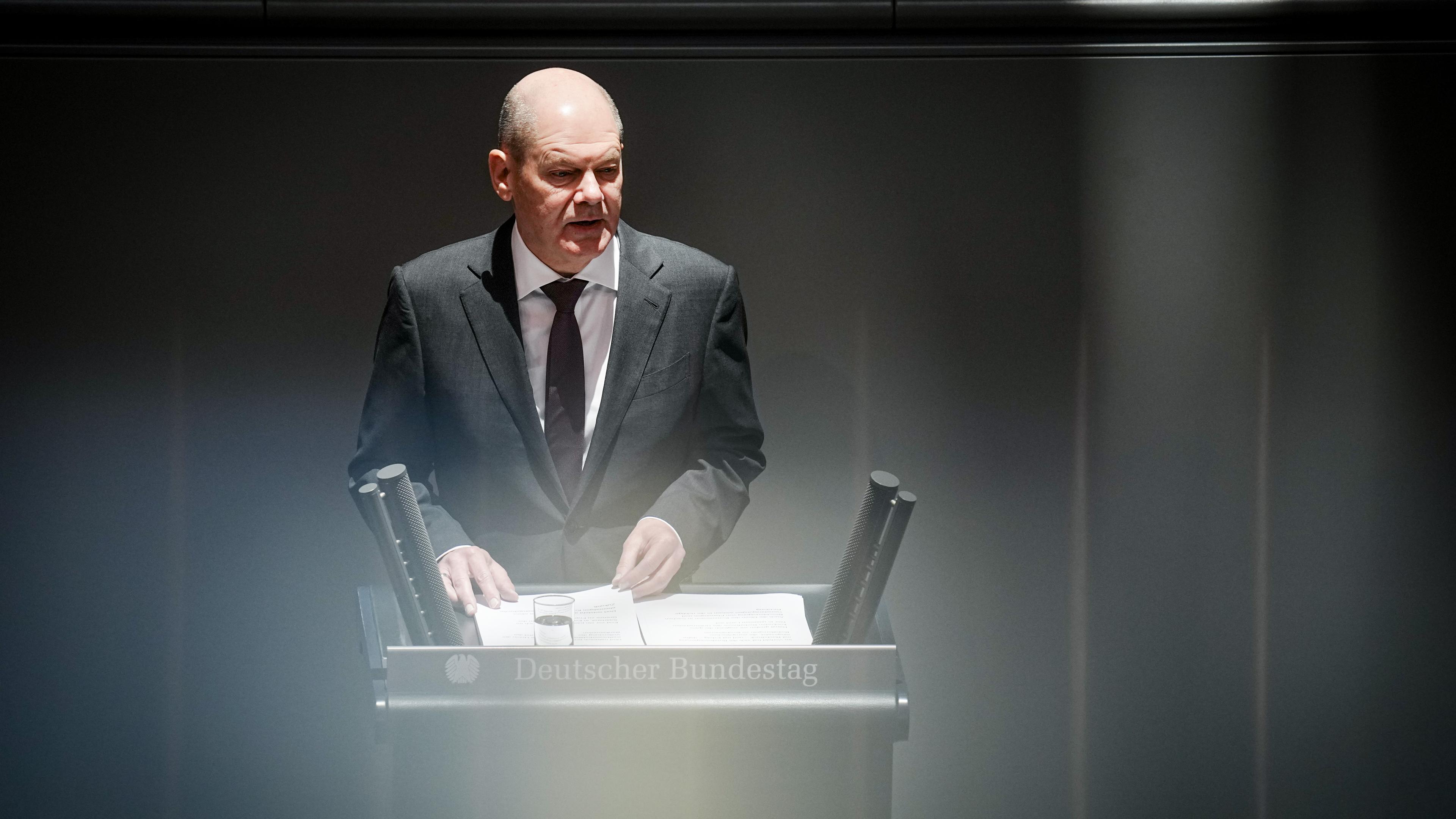 Bundeskanzler Olaf Scholz steht im schwarzen Anzug an Rednerpult im Bundestag.