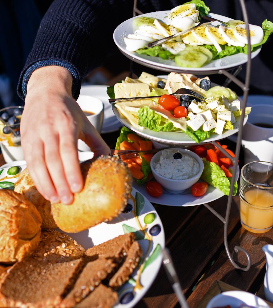Eine Schale mit Brötchen und Brot steht neben Aufstrichen und Käse, Eiern und Salat auf einem Frühstückstisch, aufgenommen am 05.03.2022