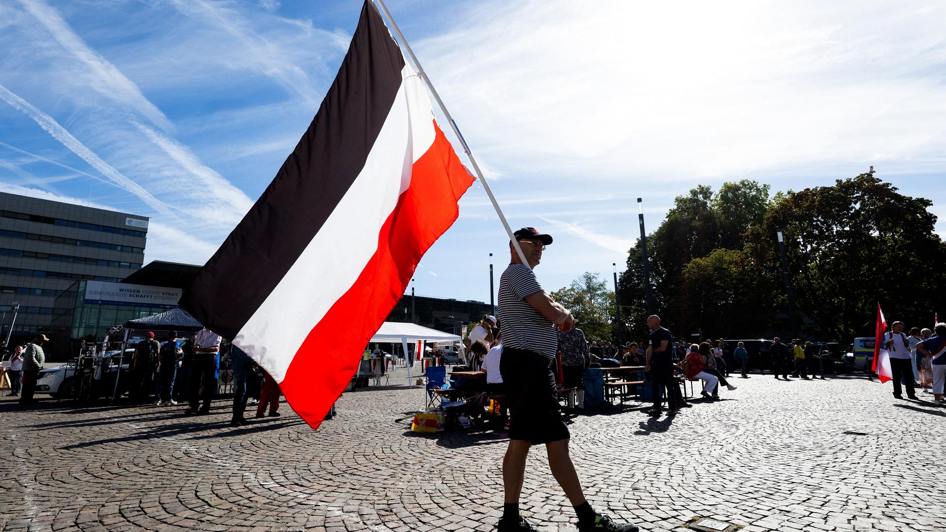Mann läuft mit Flagge des deutschen Kaiserreichs über einen Platz