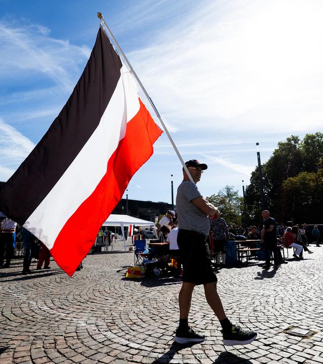 Mann läuft mit Flagge des deutschen Kaiserreichs über einen Platz