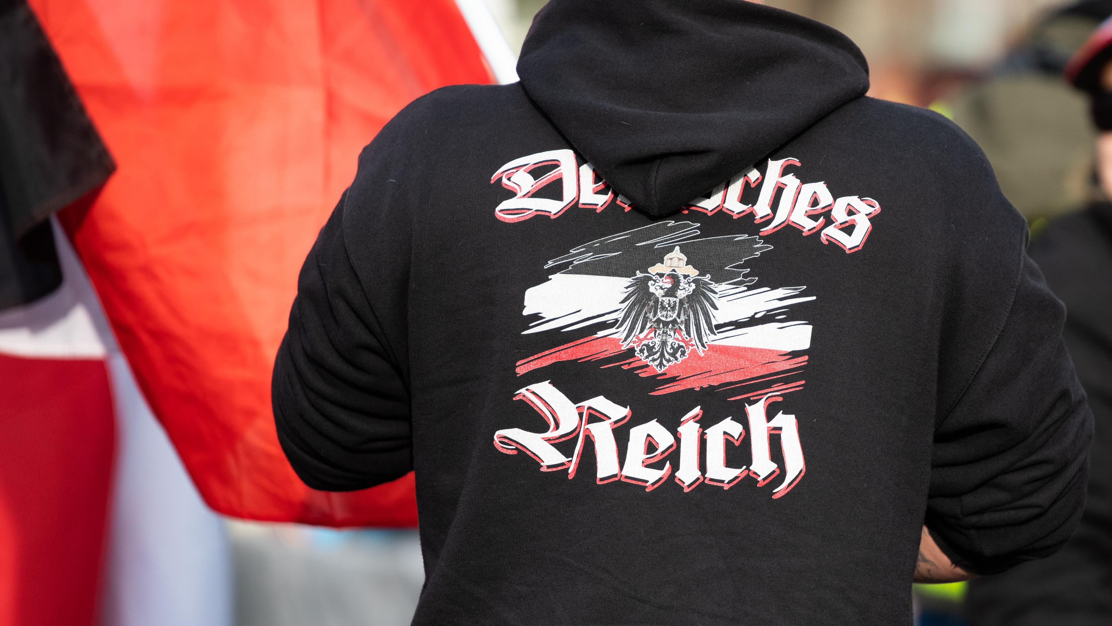 Ein Mann trägt einen Pullover mit dem Aufdruck auf der Rückseite  «Deutsches Reich» bei einer Demonstration von Reichsbürgern. 