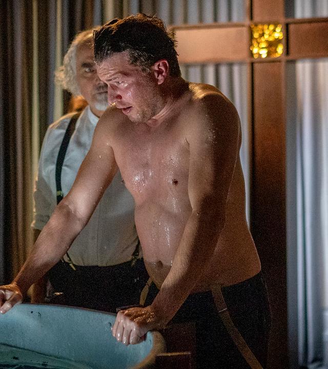 Nick Brandt (Raúl Richter) steht mit freiem Oberkörper in einem düsteren Raum. Er stützt sich mit beiden Händen an den Rand eines großen Bottiches, in dem Wasser ist. Sein Kopf und sein Oberkörper sind nass. Neben ihm steht Gideon Frey (Hansa Czypionka), der ihn ansieht. Im Hintergrund stehen zwei Frauen (Komparsen). Im Hintergrund steht ein großes Kreuz.