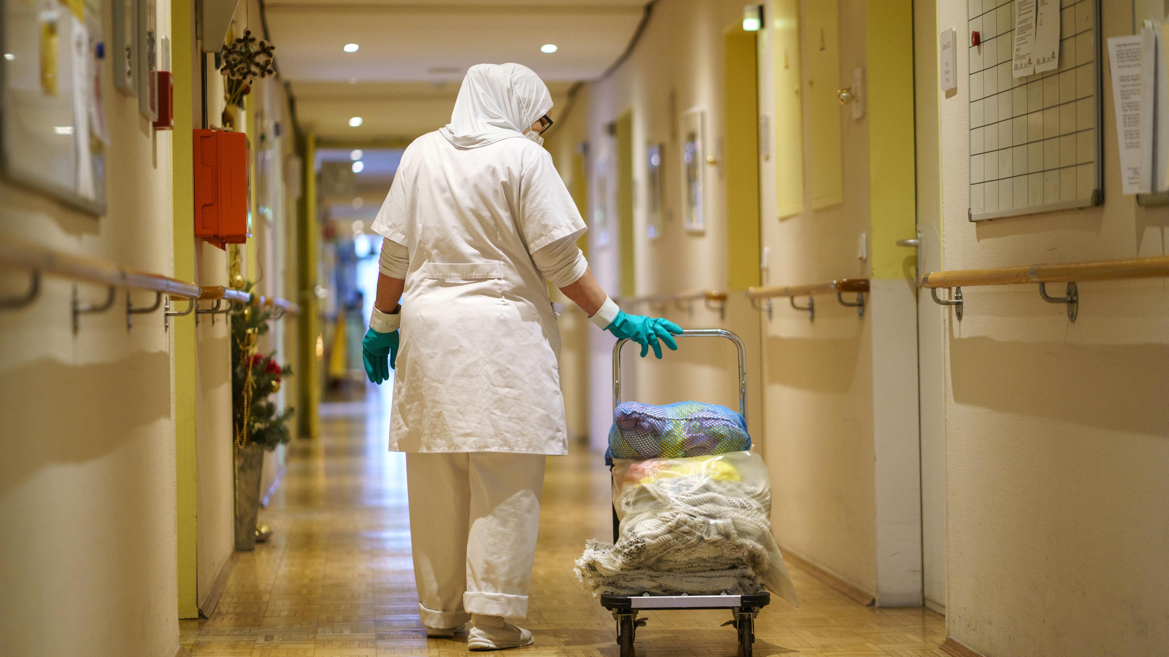 Eine Reinigungskraft zieht einen Wagen mit Wäsche einen der Gänge eines Alten- und Pflegeheims.