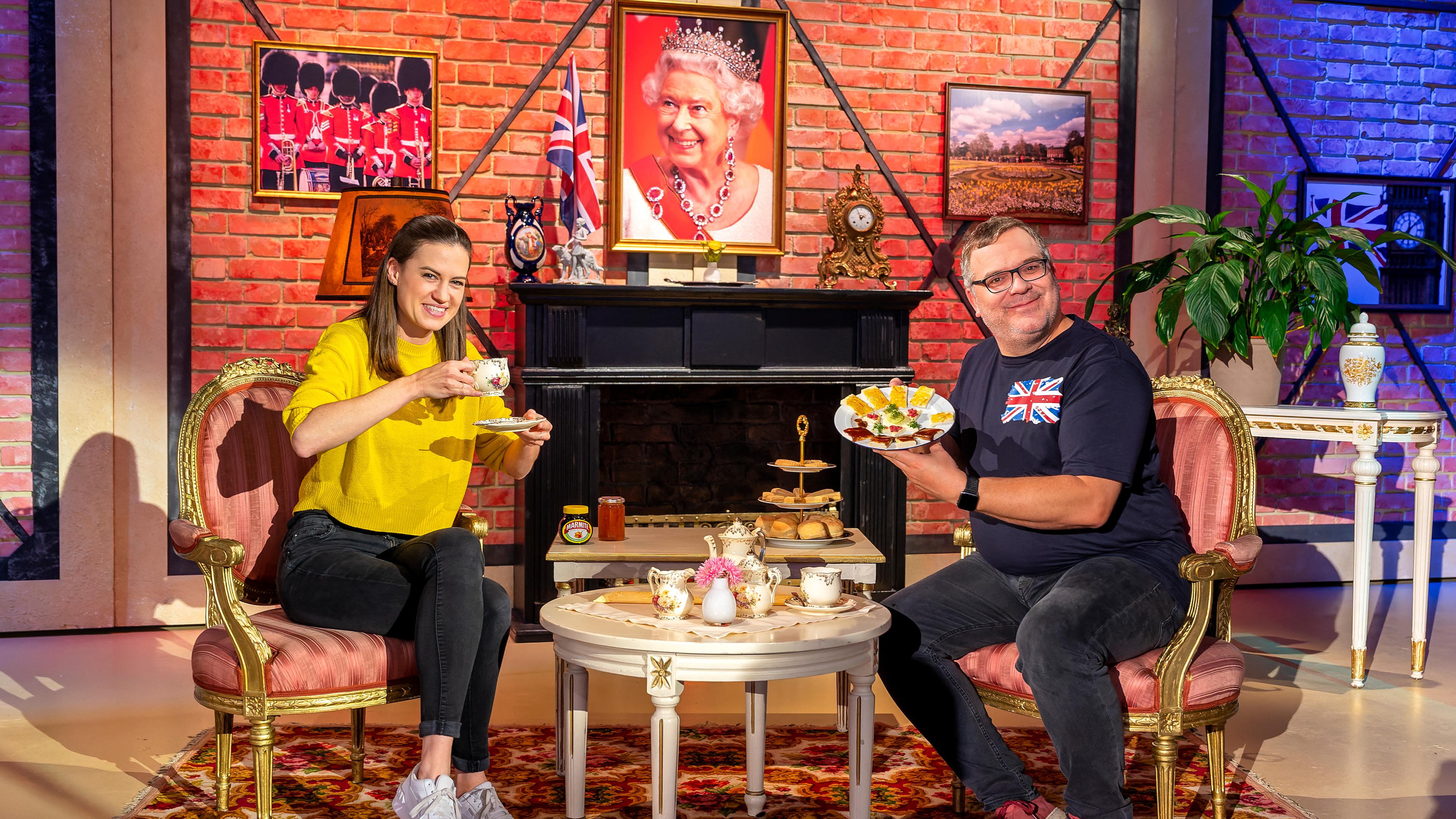1, 2 oder 3: Moderator Elton sitzt mit Studiogästin Rachel Stewart im "1, 2 oder 3"-Studio vor einem Porträt der Queen. Zwischen ihnen befinden sich Tee und englische Snacks.