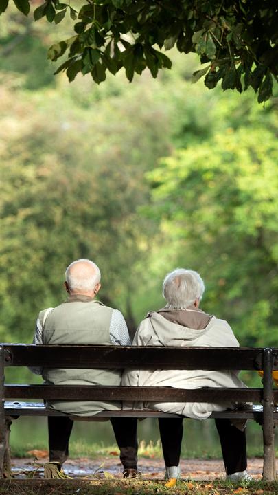 Zu sehen sind zwei betagte Menschen auf einer Parkbank.