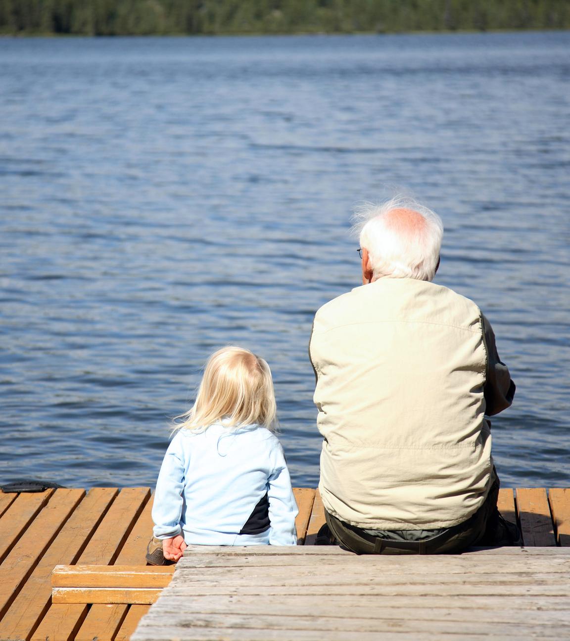 Großvater und Enkelin sitzen am Ufer eines Sees