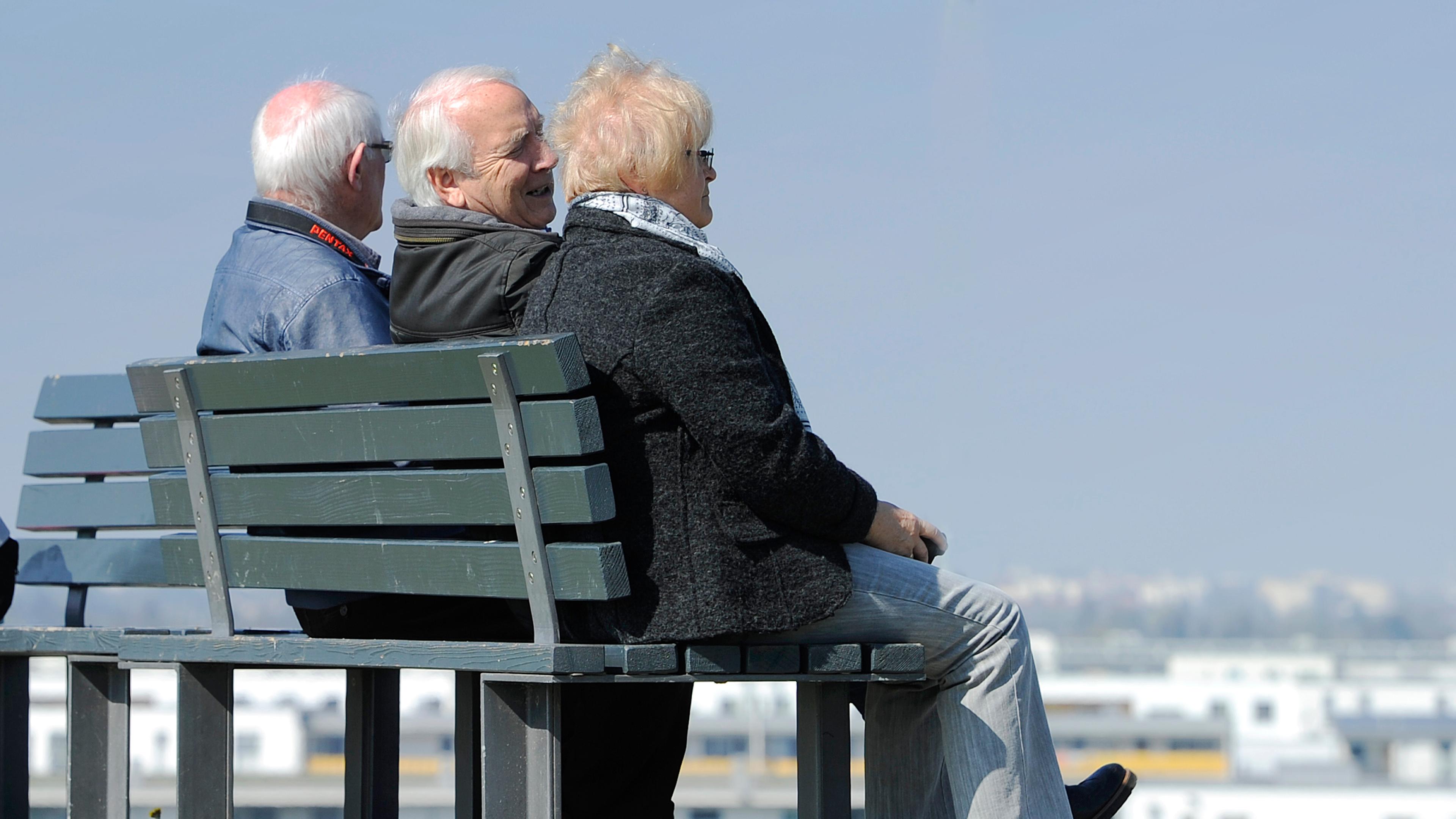 Drei Rentner sitzen auf einer Bank und schauen in die Ferne.