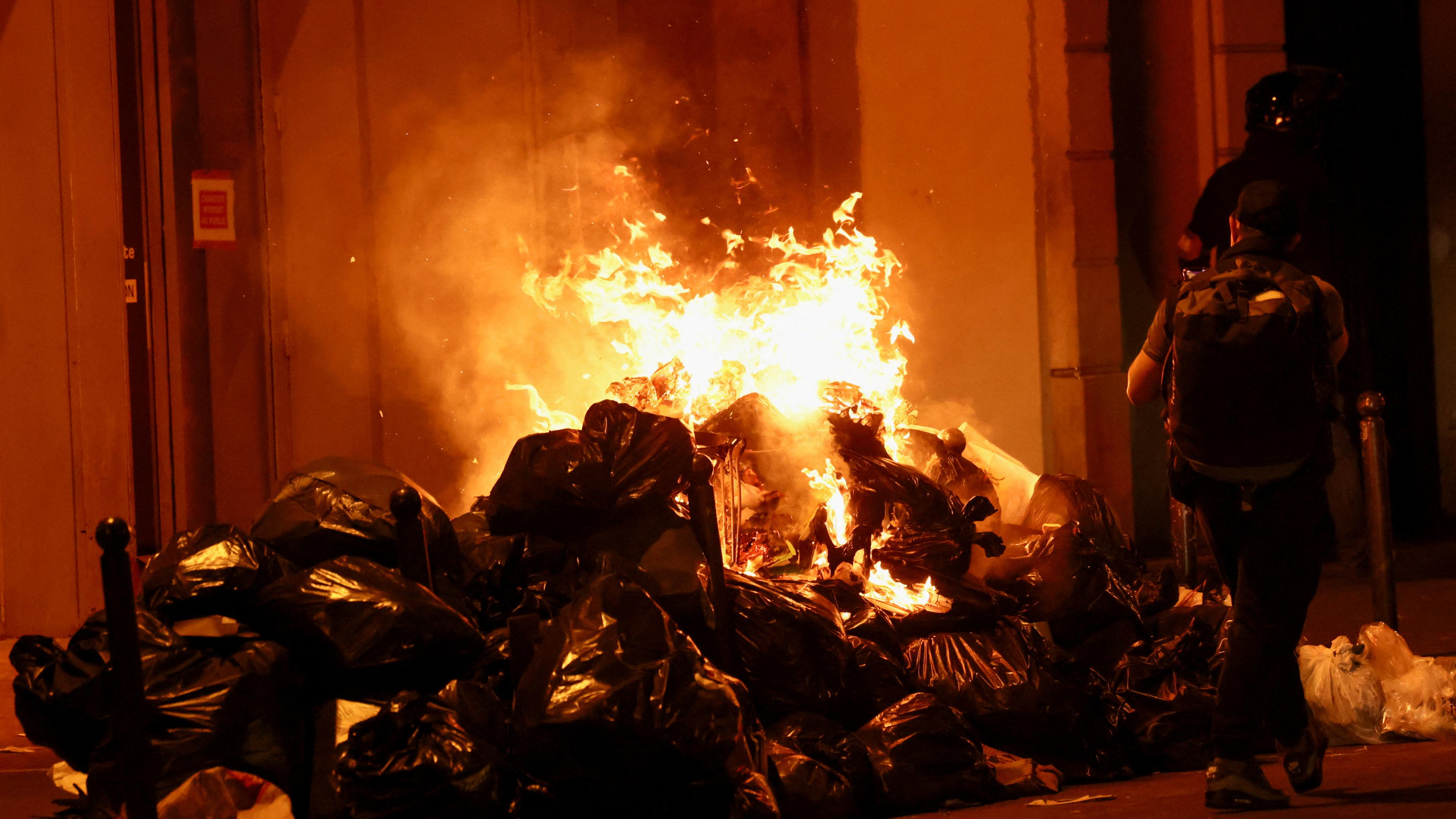 Eine Person läuft an brennenden Müllsäcken in Paris vorbei. 