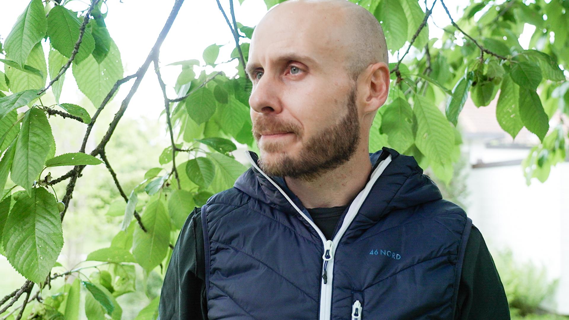 Lukas Bissegger vor Zweigen mit grünen Blättern.