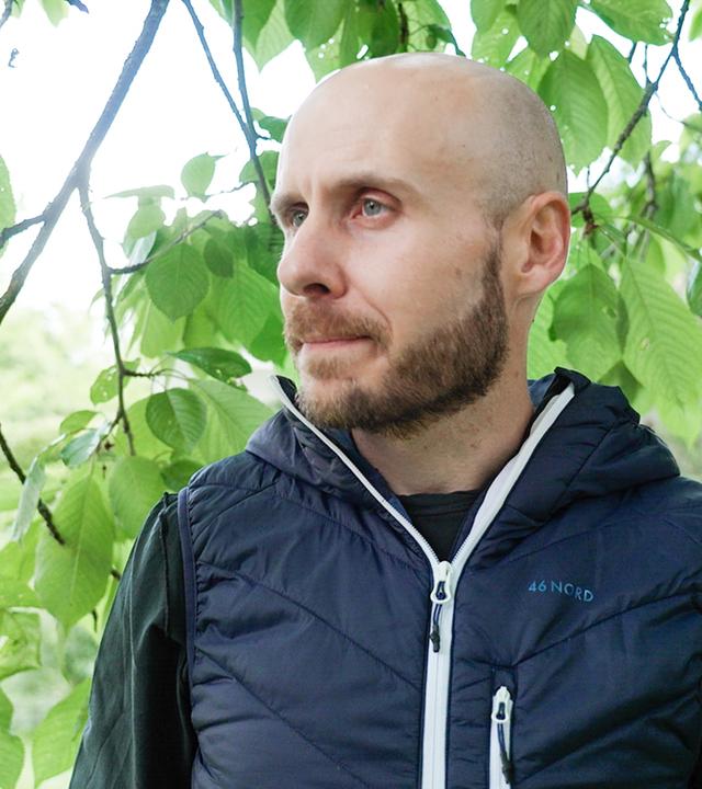 Lukas Bissegger vor Zweigen mit grünen Blättern.