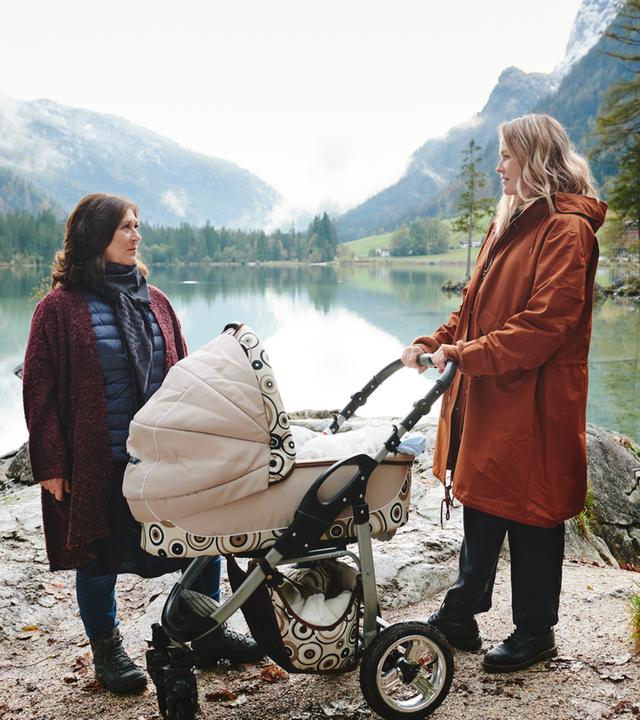 "Lena Lorenz - Retterbaby": An einem See in Berglandschaft stehen Eva (Eva Mattes) und Lena Lorenz (Judith Hoersch) mit Kinderwagen und schauen sich an.
