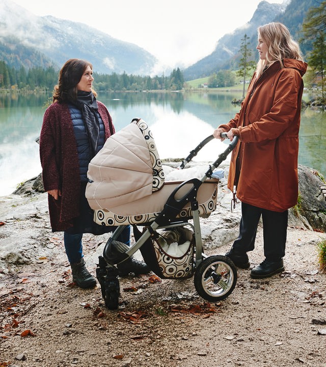 "Lena Lorenz - Retterbaby": An einem See in Berglandschaft stehen Eva (Eva Mattes) und Lena Lorenz (Judith Hoersch) mit Kinderwagen und schauen sich an.