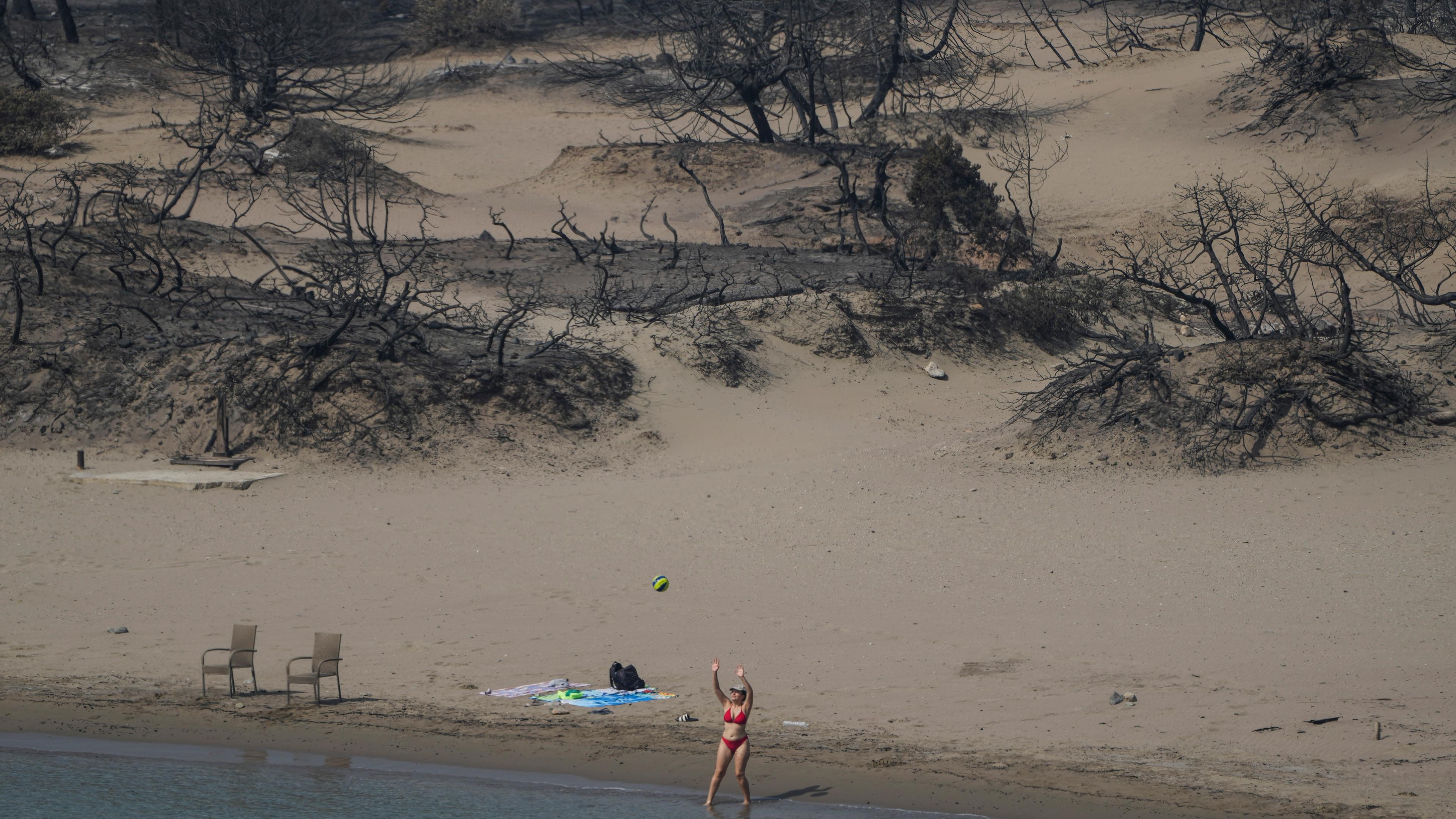Griechenland, Rhodos: Eine Frau spielt mit einem Ball vor einem verbrannten Wald an einem Strand in der Nähe des Dorfes Gennadi.