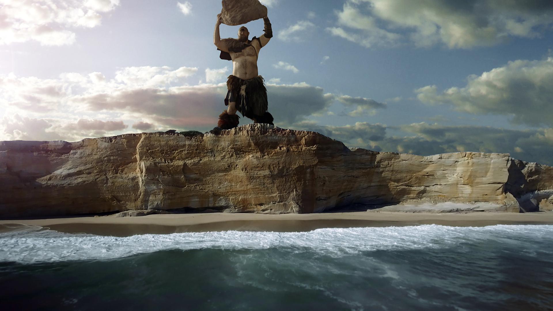 Der Riese Polyphem steht an einer Klippe und hält einen großen Stein, den er ins Meer werfen will.