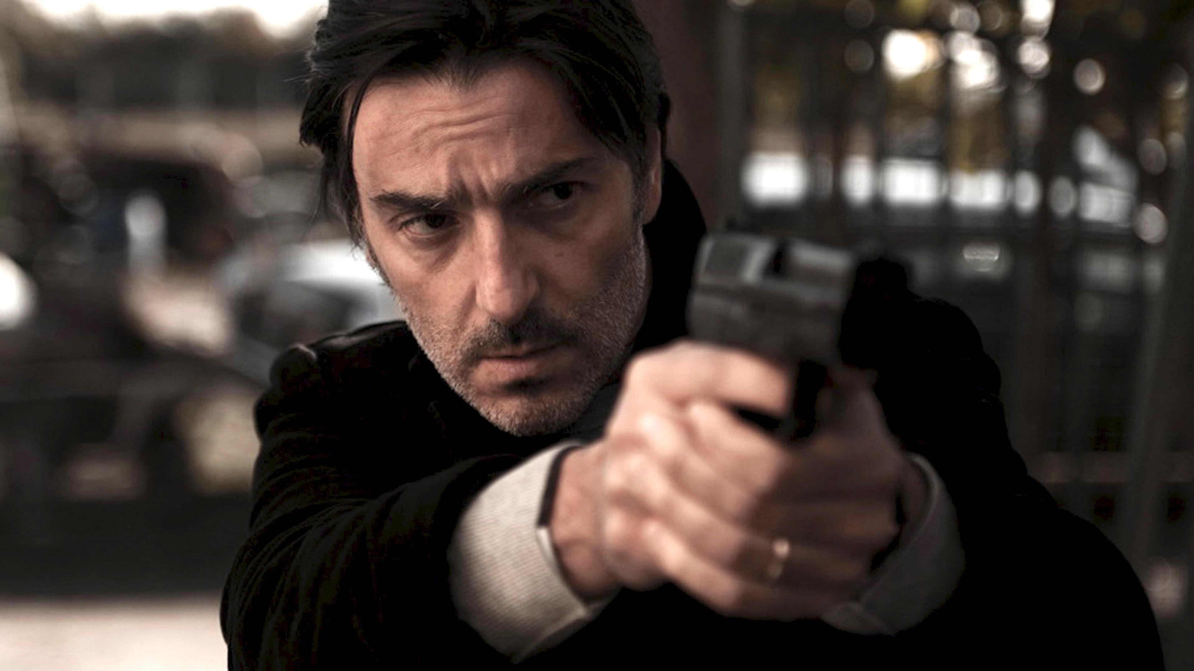 Stéphane (Yvan Attal) visiert mit der Pistole sein Ziel an.