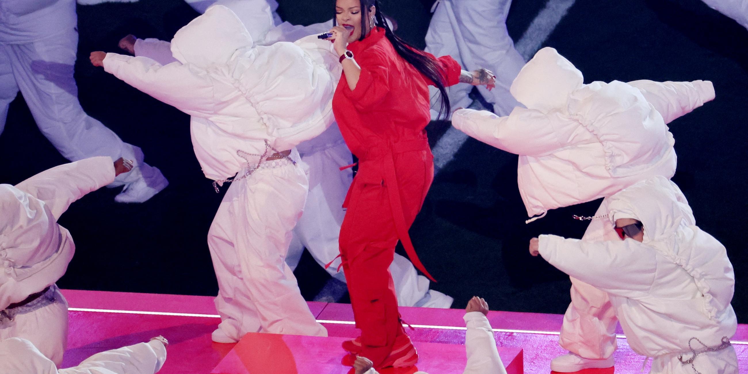 Rihanna in rot gekleidet singt beim Superbowl auf der Bühne, umgeben von Tänzern in weiß gekleidet