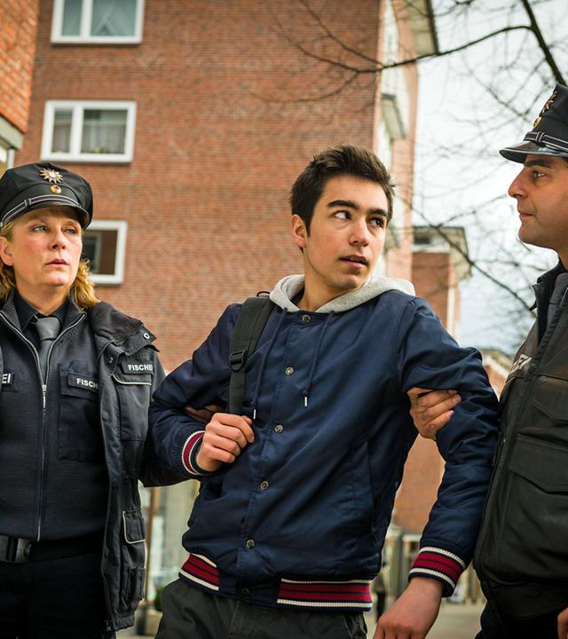 "Notruf Hafenkante - Ringo, Kim und Sidney": Ringo (Tan Julius Ipekkaya) steht zwischen den Polizisten Claudia Fischer (Janette Rauch) und Tarik Coban (Serhat Cokgezen), die ihn an den Armen festhalten. Tarik sieht den Jungen böse an.