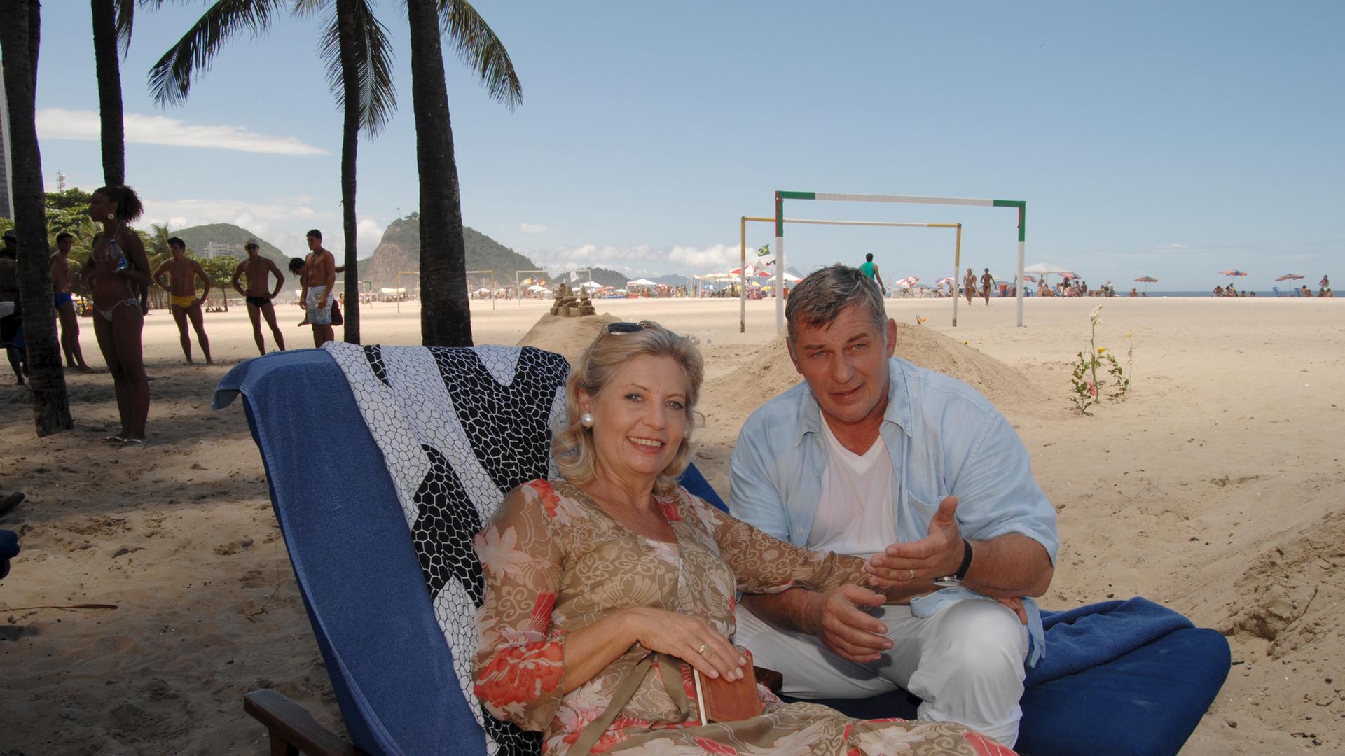 "Das Traumschiff: Rio de Janeiro": Auf Liegestühlen sitzen Brigitte (Sabine Postel) und Paul Eisfeld (Heinz Hönig) nebeneinander am Strand und lachen in die Kamera
