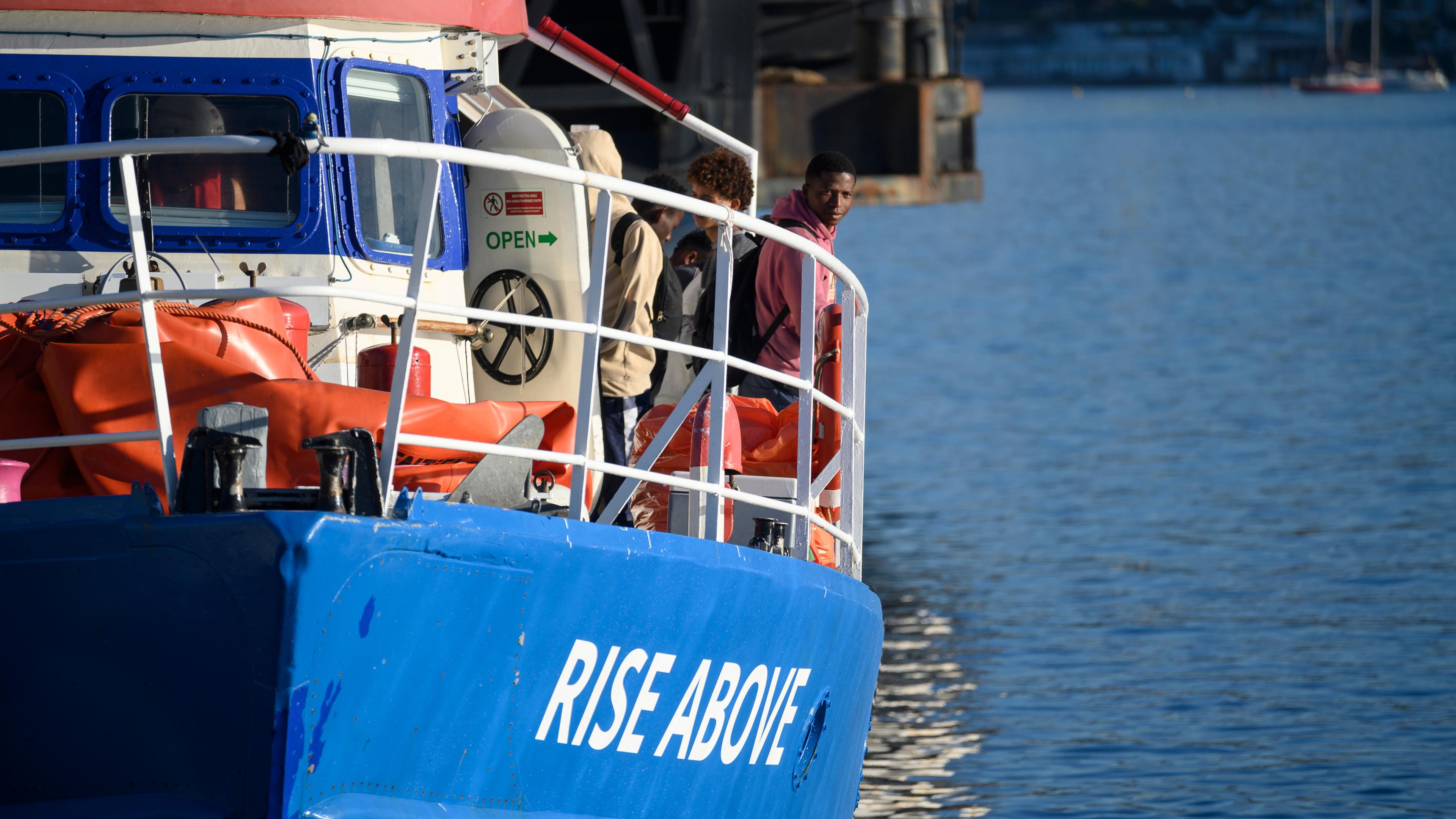 Italien, Reggio Calabria: Migranten schauen aus dem deutschen humanitären Schiff "Rise Above" heraus, als sie in der süditalienischen Hafenstadt Reggio Calabria anlegen.