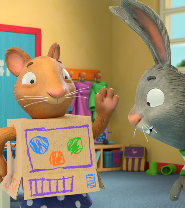 Posy trägt ihr Roboterkostüm, das aus einem bunt bemalten Karton besteht. Pip schaut sich das Kostüm genau an.