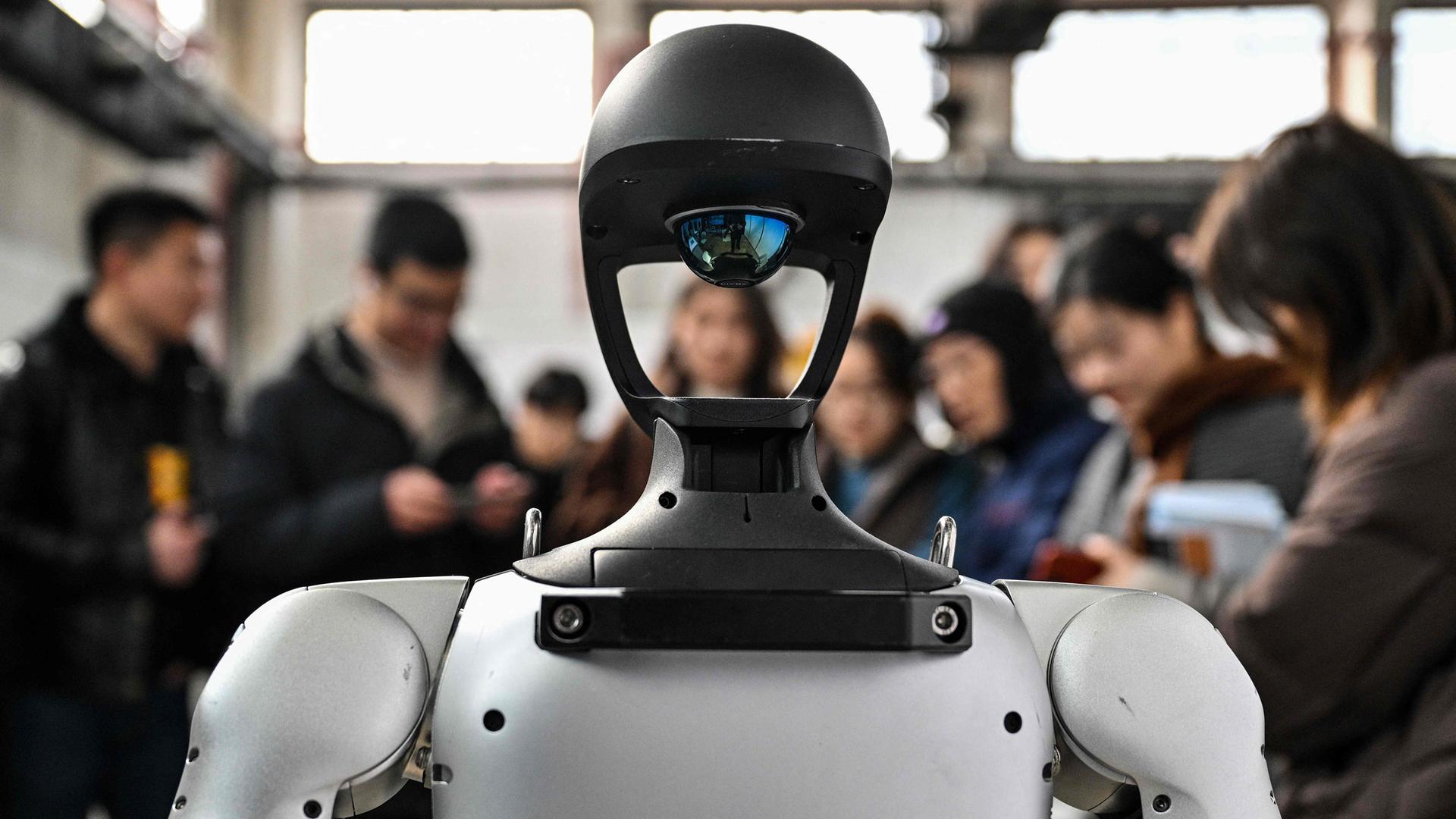 Ein humanoider Roboter wird bei einer Messe von Menschen umringt, die ihn betrachten.