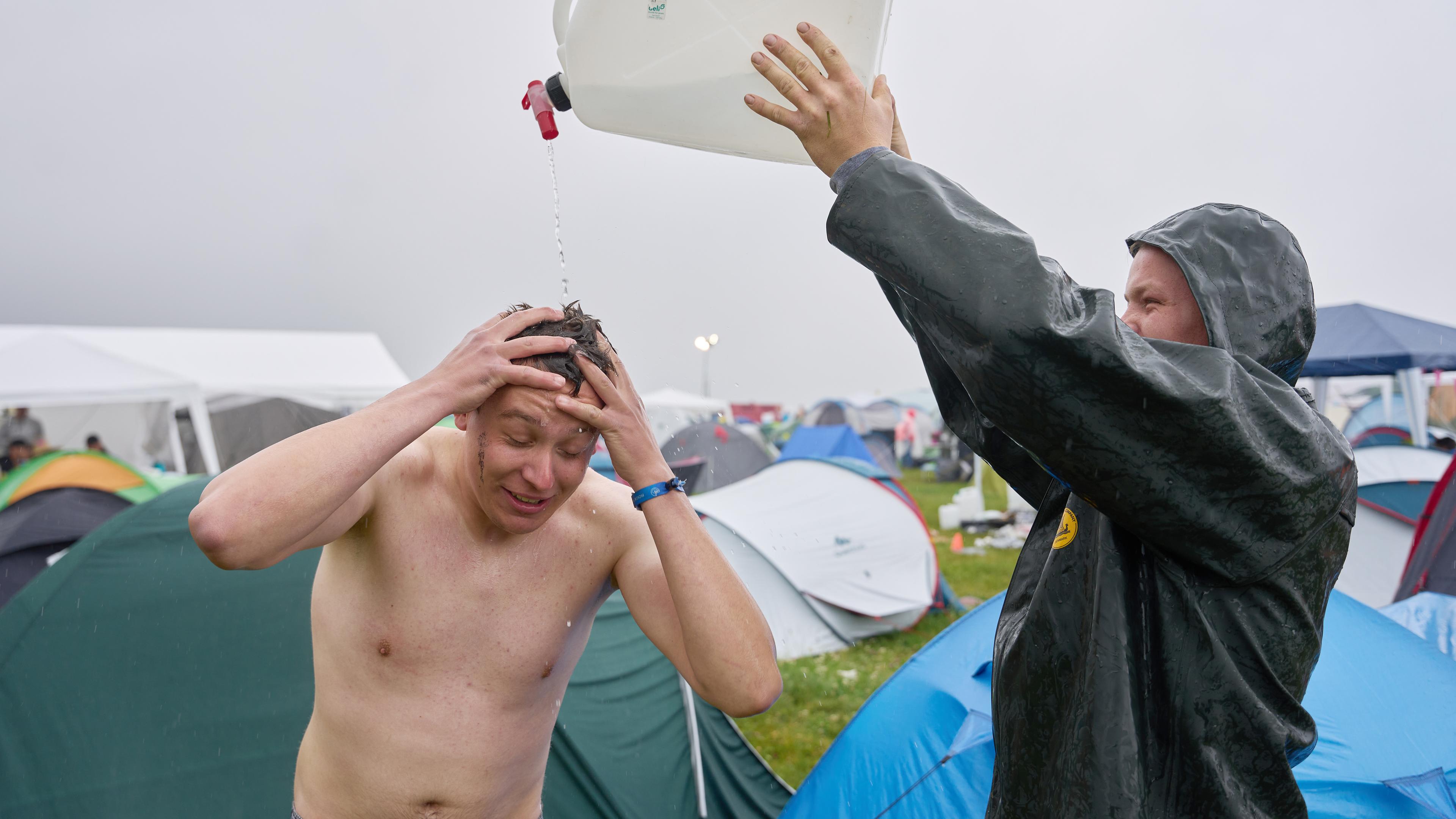 Rheinland-Pfalz, Nürburg: Thomas aus dem Sauerland duscht auf dem Camping gelände des Festivals "Rock am Ring". trotz Regens unter einem Wasserkanister. 
