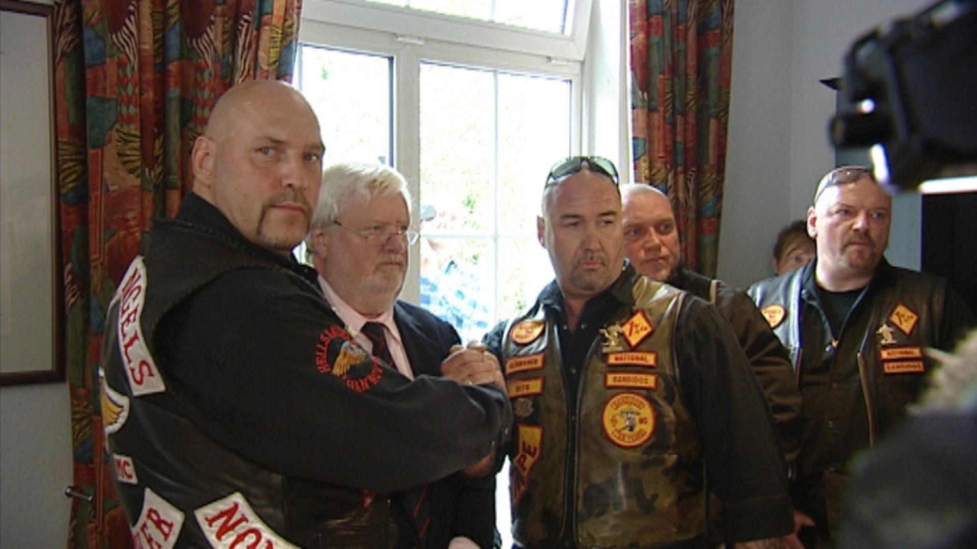 "Rockerkrieg - Neue Fronten": Die beiden Vorsitzenden der Rockerclubs Hells Angels und Bandidos geben sich vor der Kamera die Hand. Hinter ihnen stehen weitere Personen.