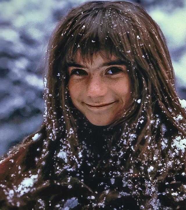 Außenaufnahme. Ronja (Hanna Zetterberg) steht lächelnd da und ist mit Schnee bedeckt.