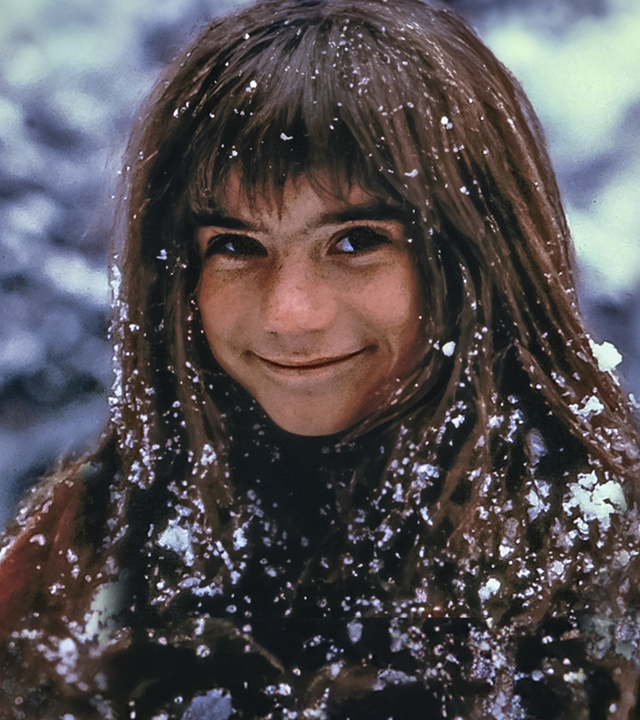 Außenaufnahme. Ronja (Hanna Zetterberg) steht lächelnd da und ist mit Schnee bedeckt.