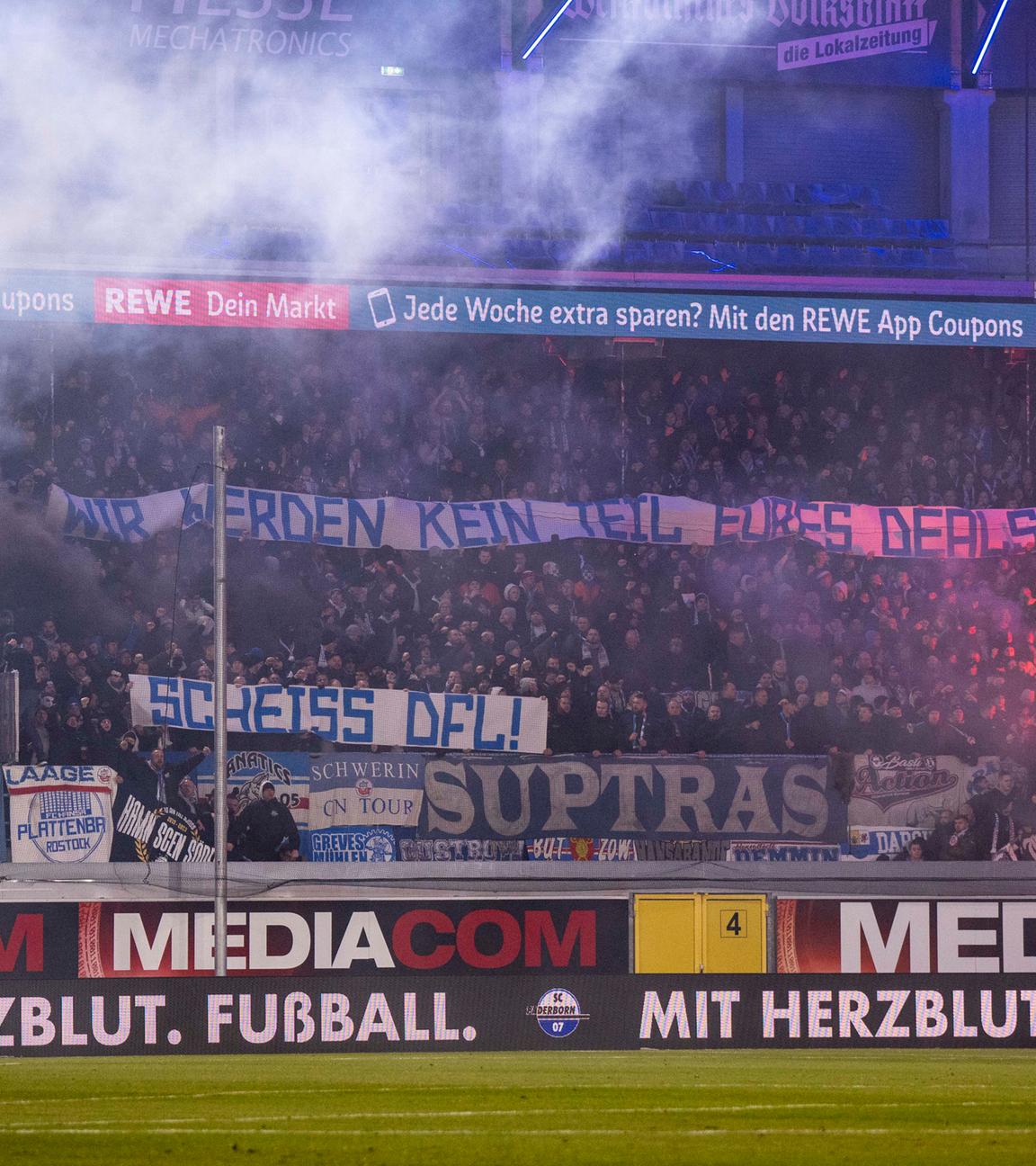 Rostocker Fans protestieren mit Bannern und Pyrotechnik gegen die DFL und Investoren am 15.12.2023.