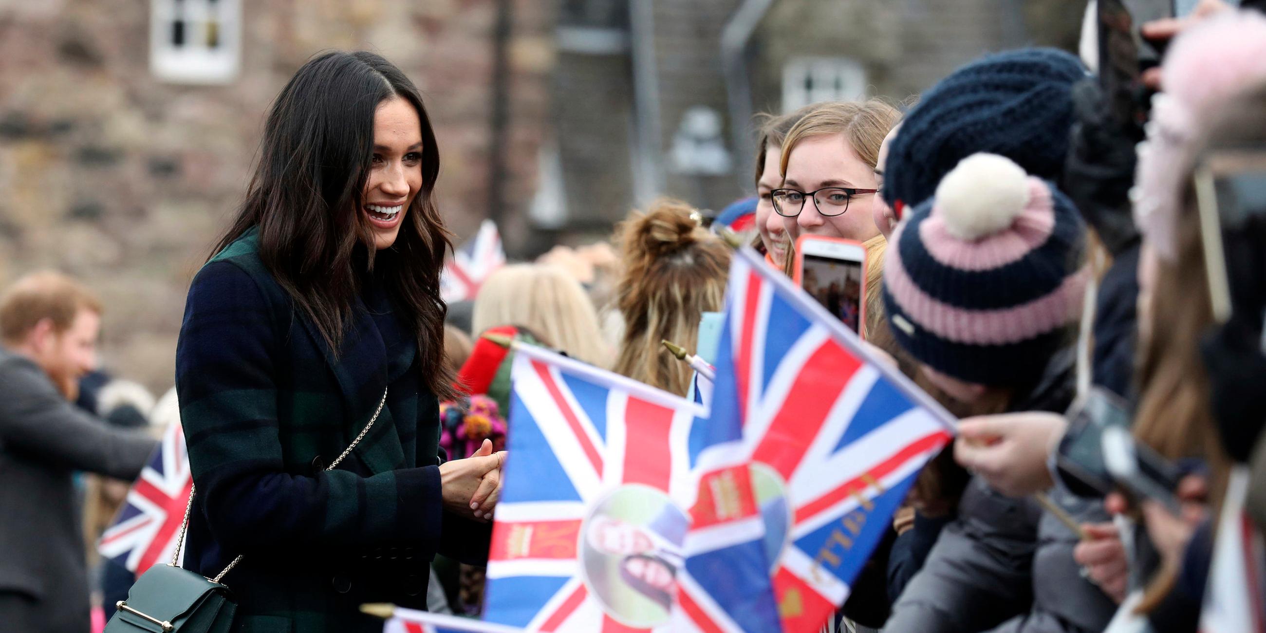 Das Bild zeigt Herzogin Meghan mit Fans des britischen Königshauses, die Union-Jack-Flaggen halten.