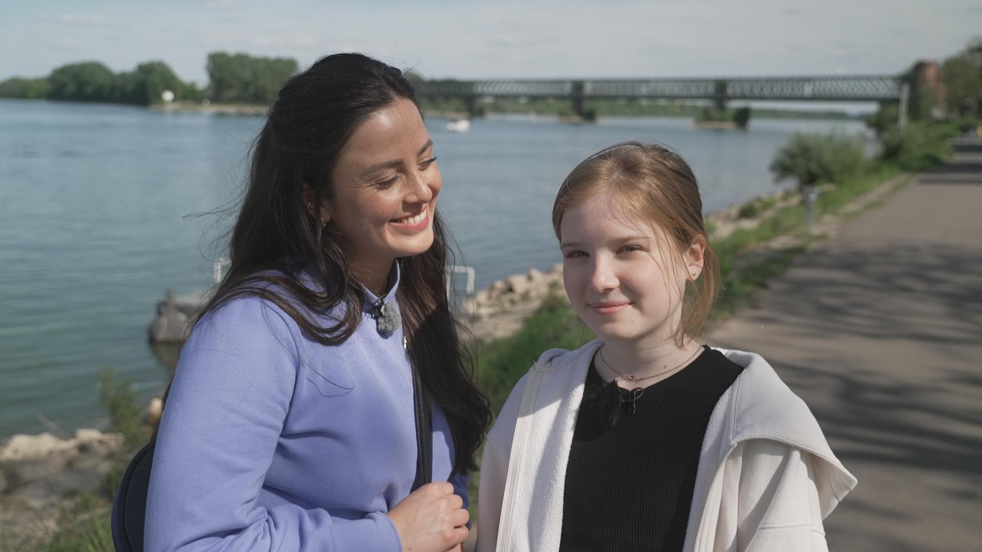 logo!-Reporterin Teresa lächelt die 14-jährige Amelie an. Sie stehen Rhein und die Sonne scheint. 