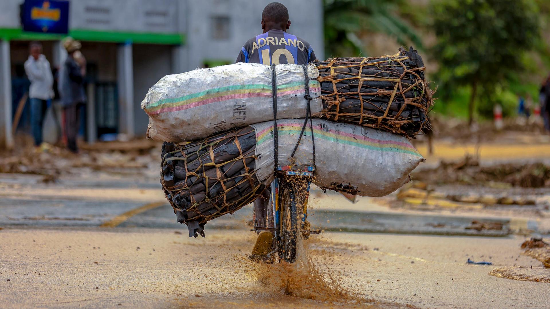 Ruanda, Bezirk Karongi: Ein Mann, der Holzkohle auf einem Fahrrad transportiert, fährt durch Hochwasser im Bezirk Karongi im Westen Ruandas. 