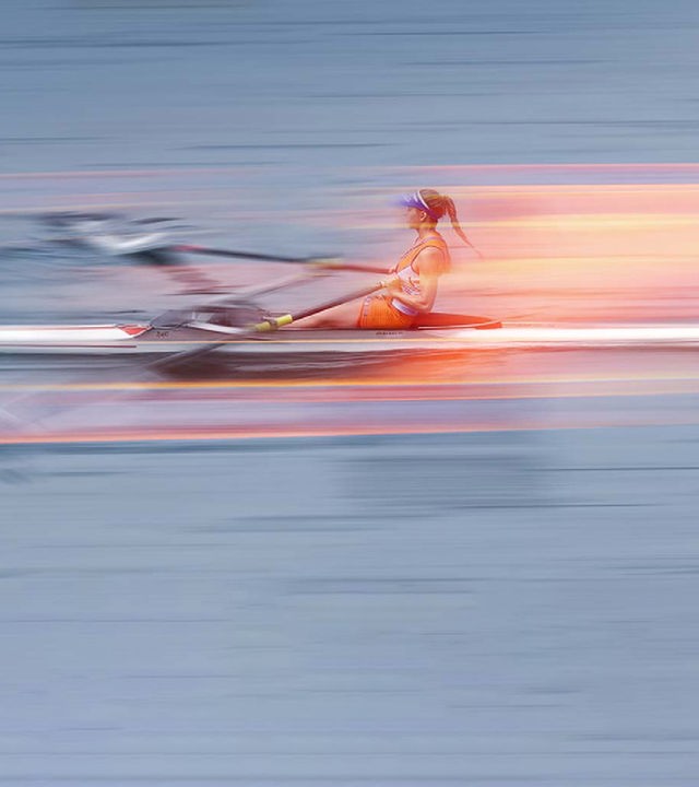 Eine Ruderin im Boot auf dem Wasser, stilistisch verfremdet um Schnelligkeit anzudeuten.