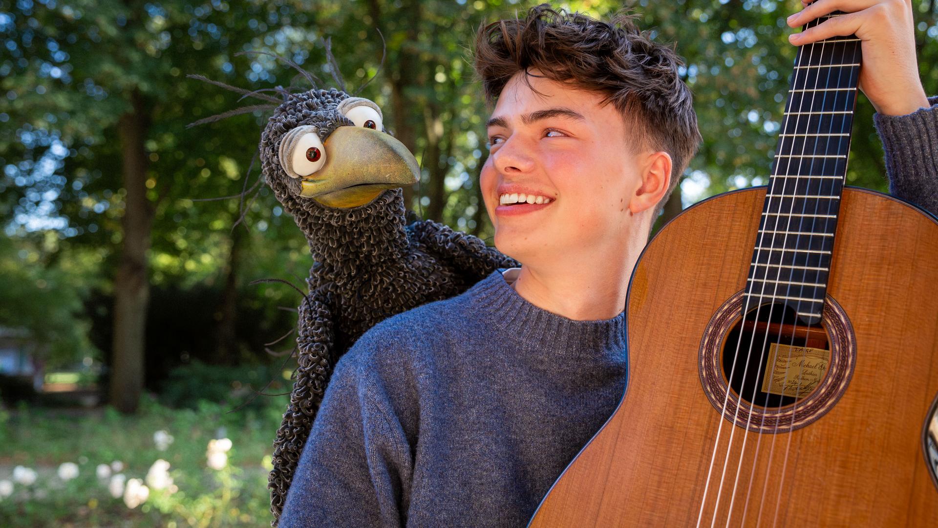 Rudi hockt auf der Schulter von Benno Panhans, der eine Gitarre hält und Rudi anlächelt.