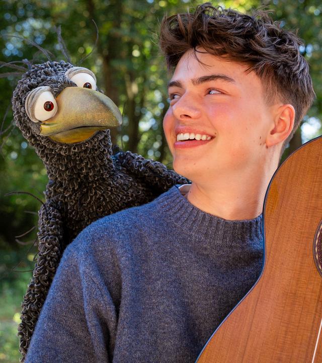 Rudi hockt auf der Schulter von Benno Panhans, der eine Gitarre hält und Rudi anlächelt.