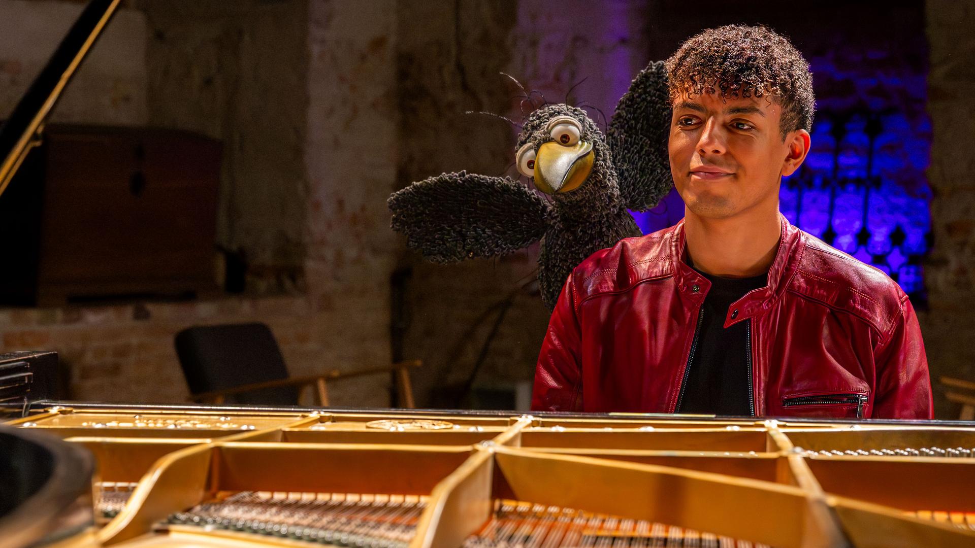 Blick durch den Flügel: Louis Philippson und Rudi sitzen hinter dem Flügel und schauen freudig in die Kamera. Rudi hebt dabei seine Flügel.