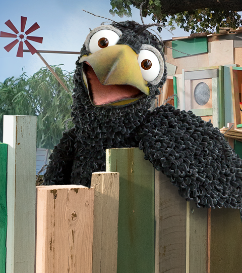 Rabe Rudi vor seinem bunt zusammengezimmerten, schiefen Holzhaus