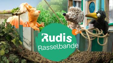 Rabe Rudi vor seinem bunt zusammengezimmerten, schiefen Holzhaus