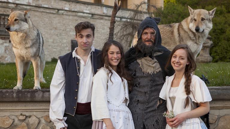 Vor dem Hintergrund der Mauern eines Schlossgartens stehen – mit Blick zum Betrachter – vier Schauspieler. Wir sehen, von links nach rechts: den in Hose mit breitem Hosenbund, weitem Hemd und dunkler Weste gekleideten Frieder, einen jungen Schlossangestellten; neben ihm die ebenso junge Magd Rosa im Kostüm aus weitem Rock, Schürze und Weste mit Lochstickereien; daneben der hünenhafte Rübezahl - bärtig, verdreckt, alterslos und im groben schwarzen Tuch samt Kapuze und riesigem Holzstecken verkleidet als ein Vagabund; und schließlich Klärchen, ebenfalls blutjung und im Mägdekostüm, mit zwei Blütenzweigen in der Hand. Die Szene wird rechts und links flankiert von zwei ausgewachsenen braun-weißen Wolfshunden, die erhöht auf Brusthöhe des Schauspielerensembles und auf dem Sims einer Schlossmauer stehen.