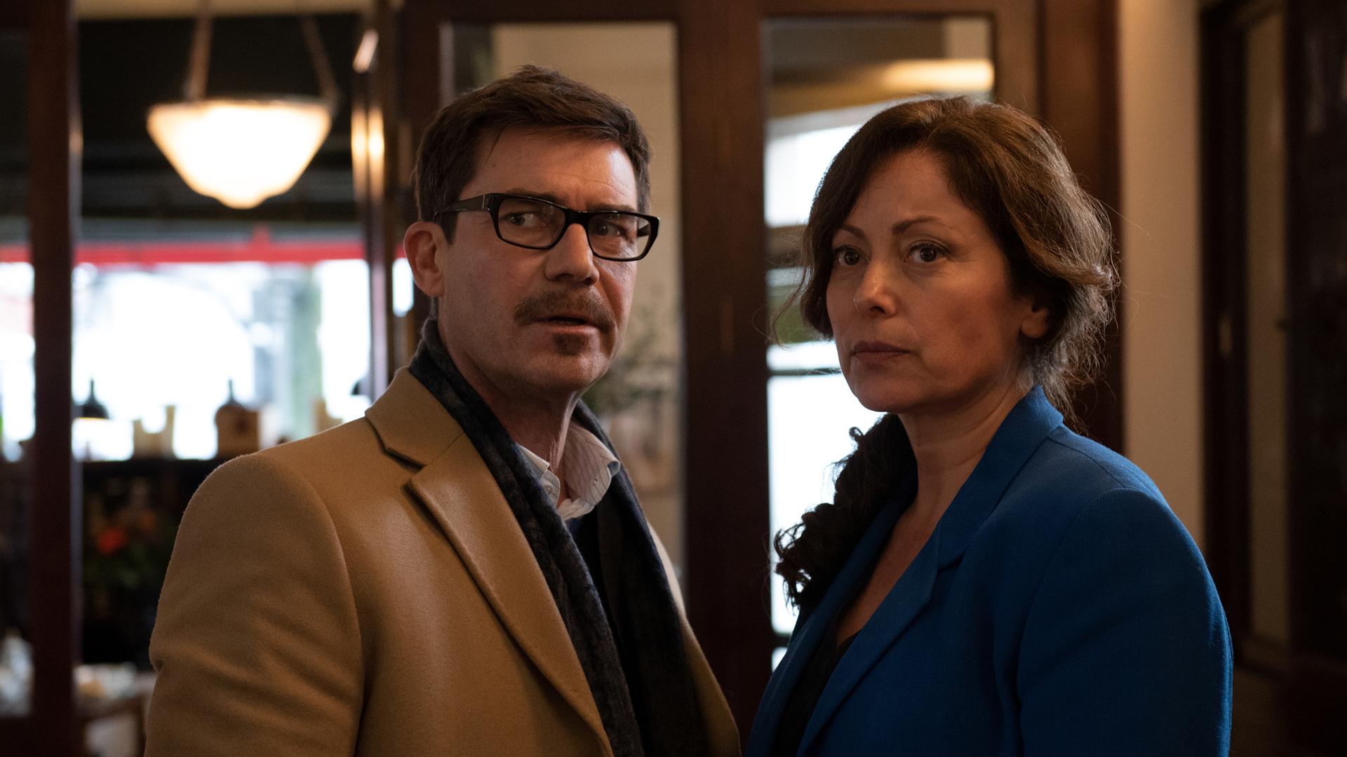 Karl Wörsching (Thomas Scharff) und Nora Wörsching (Carolina Vera) stehen in einem Flur. Beide schauen skeptisch.