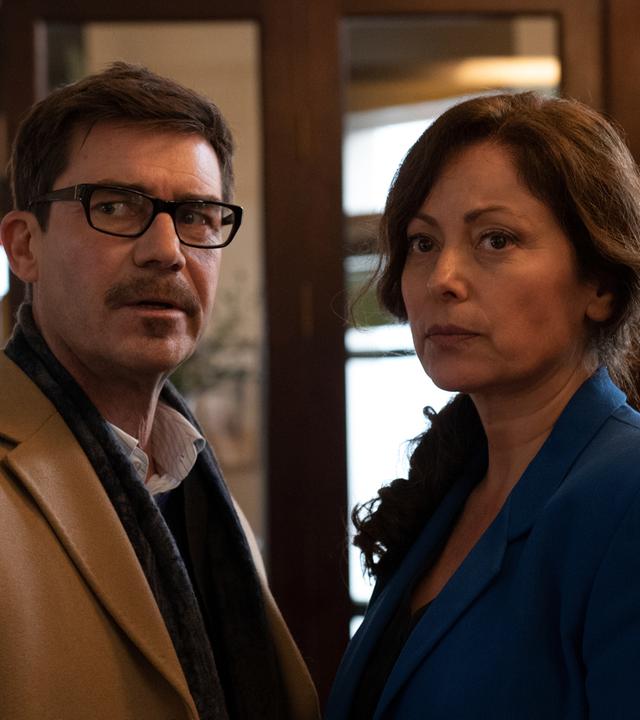 Karl Wörsching (Thomas Scharff) und Nora Wörsching (Carolina Vera) stehen in einem Flur. Beide schauen skeptisch.