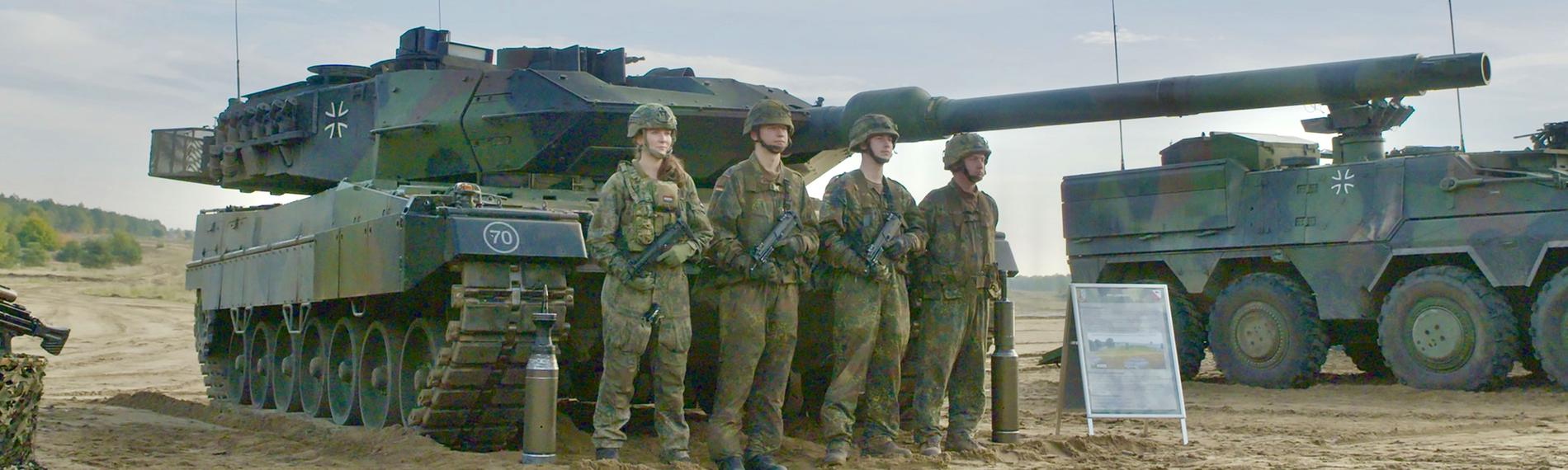 Vier Soldaten der Bundeswehr stehen in Tarnuniform vor einem Leopard 2 Panzer. Daneben steht ein weiterer Panzer.