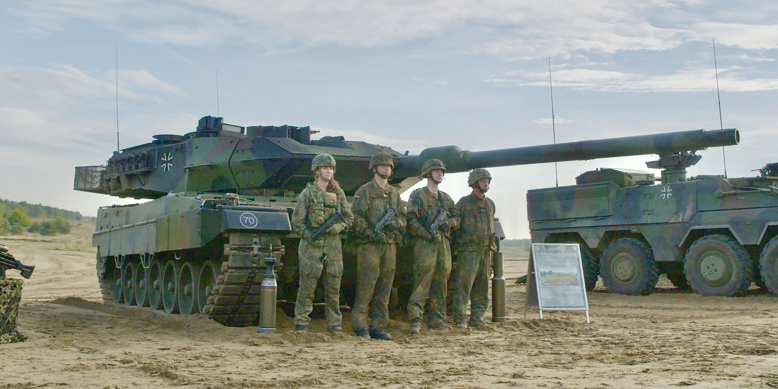 Vier Soldaten der Bundeswehr stehen in Tarnuniform vor einem Leopard 2 Panzer. Daneben steht ein weiterer Panzer.