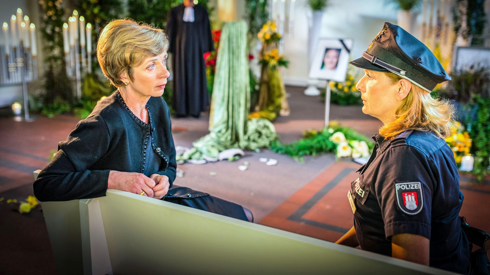 "Notruf Hafenkante - Ruhe sanft": Die Polizeibeamtin Claudia Fischer (Janette Rauch) sitzt mit der Witwe Elisabeth Höpfner (Anna Stieblich) auf einer Bank in einer Trauerhalle. Sie schauen einander an.