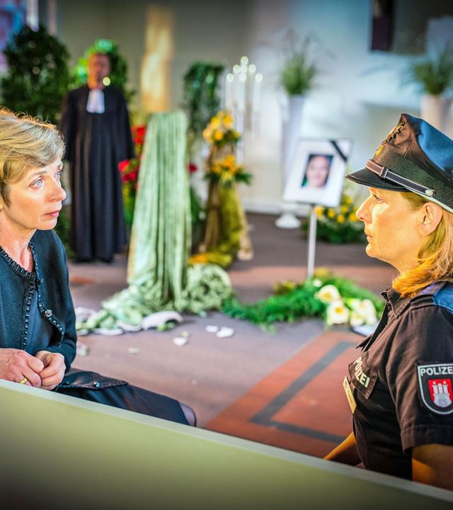 "Notruf Hafenkante - Ruhe sanft": Die Polizeibeamtin Claudia Fischer (Janette Rauch) sitzt mit der Witwe Elisabeth Höpfner (Anna Stieblich) auf einer Bank in einer Trauerhalle. Sie schauen einander an.