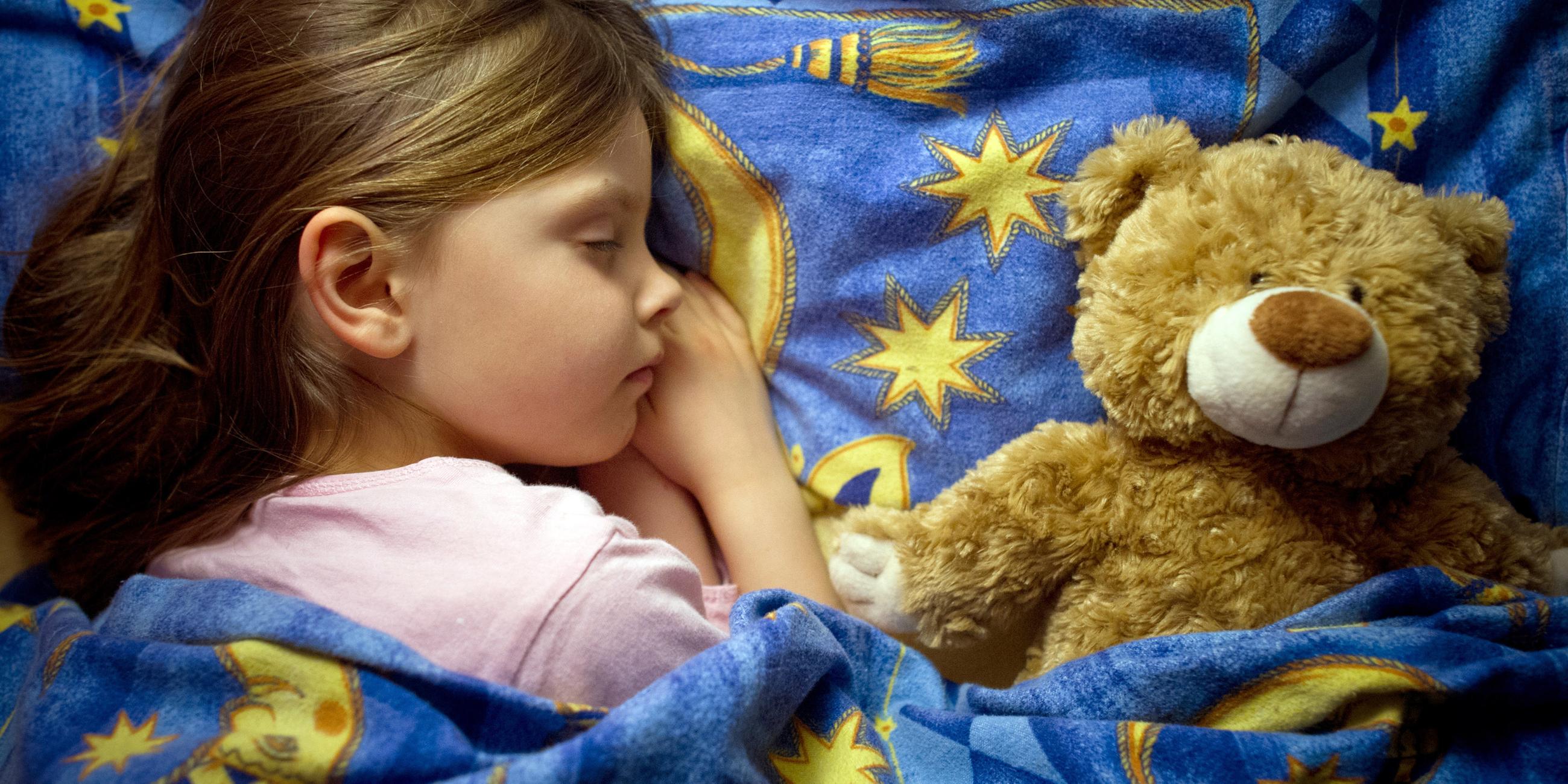 Schlafendes Kind neben einem Teddybären.